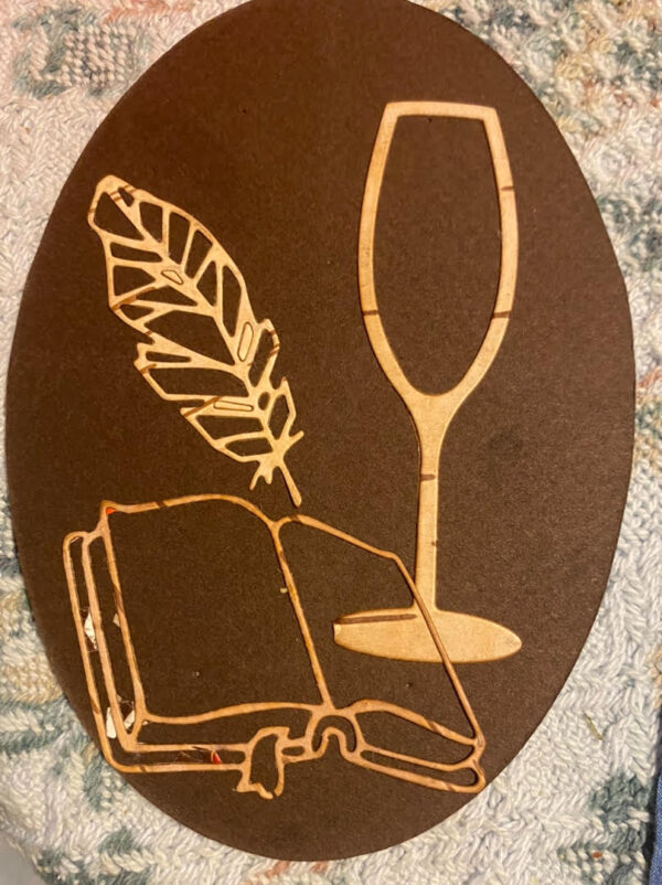 a beautiful bookmark made from birch bark, featuring a glass of wine, open book, and feather design